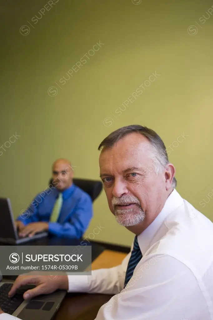 Portrait of two businessmen sitting with laptops in a meeting