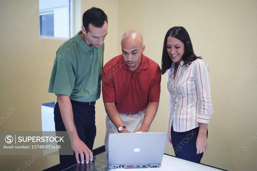 Two businessmen and a businesswoman in a discussion in front of a laptop