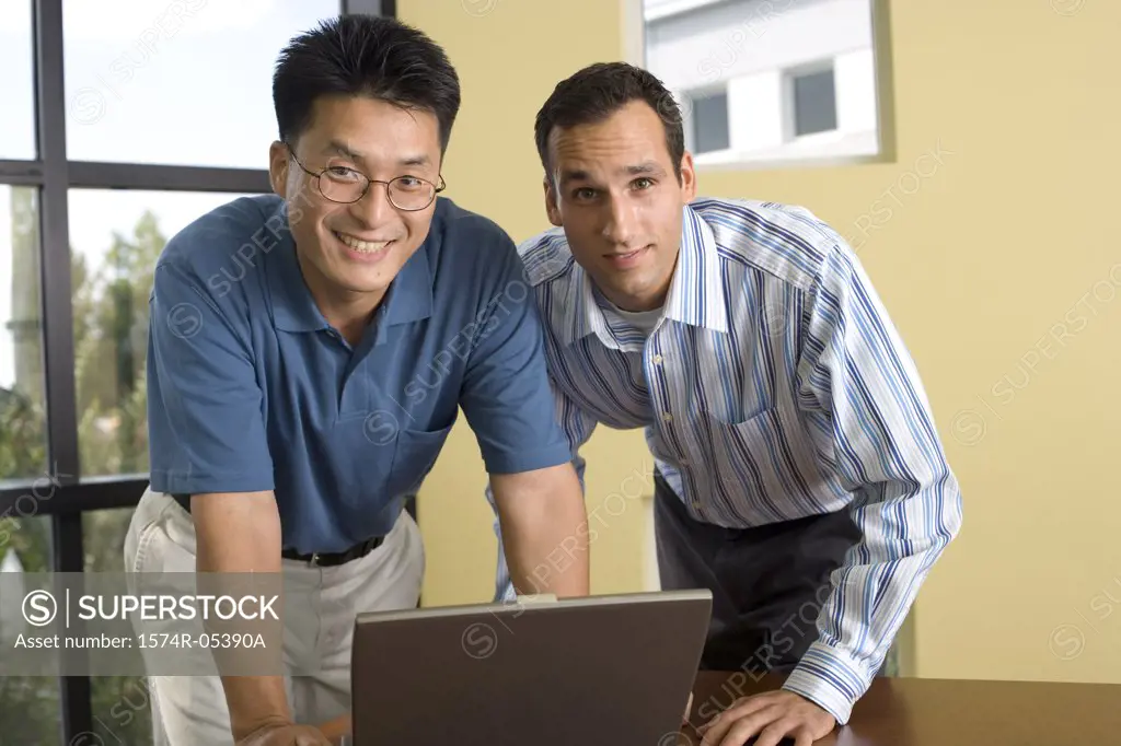 Portrait of two businessmen standing in front of a laptop