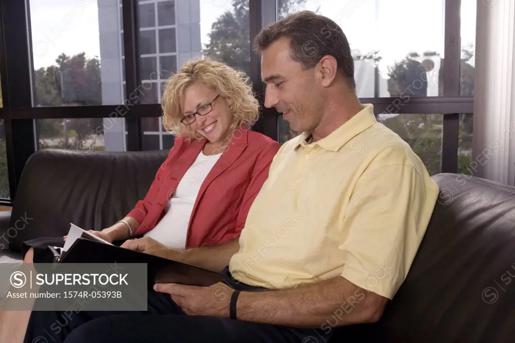 Side profile of a businessman and a businesswoman sitting on a couch reading a document