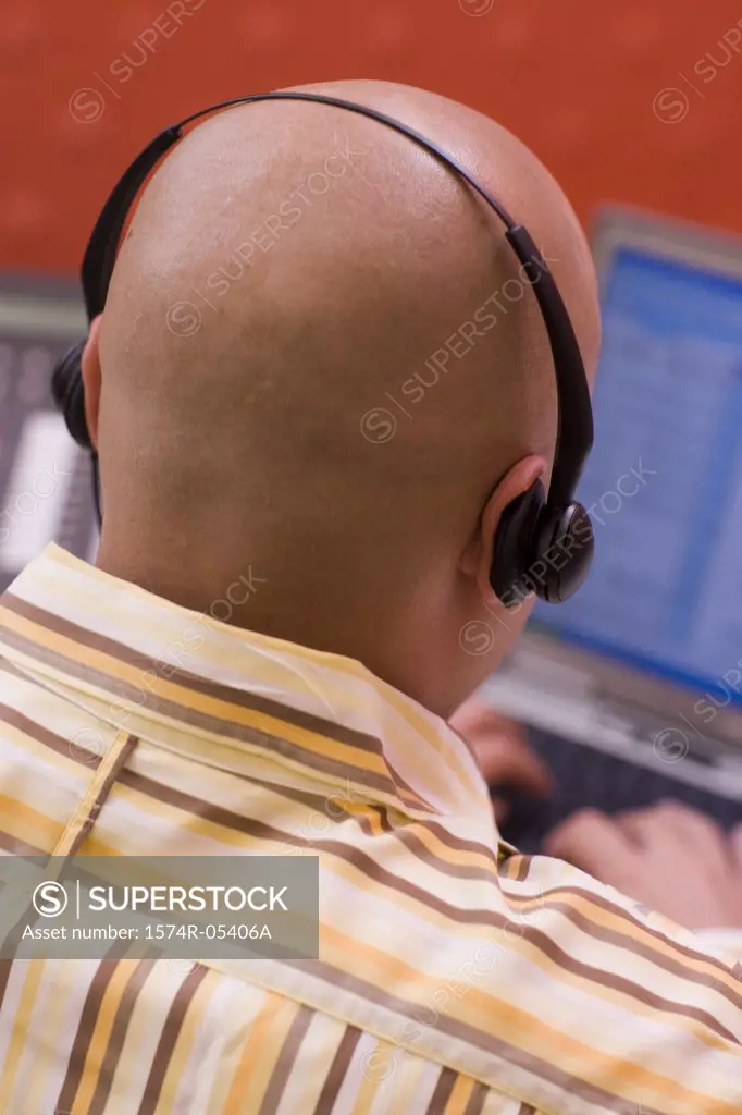 Rear view of a male customer service representative wearing a headset sitting in front of a laptop