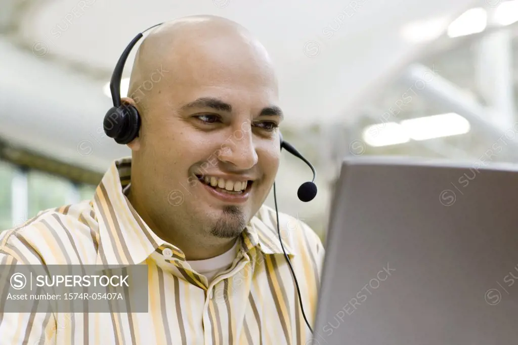 Close-up of a male customer service representative wearing a headset sitting in front of a laptop