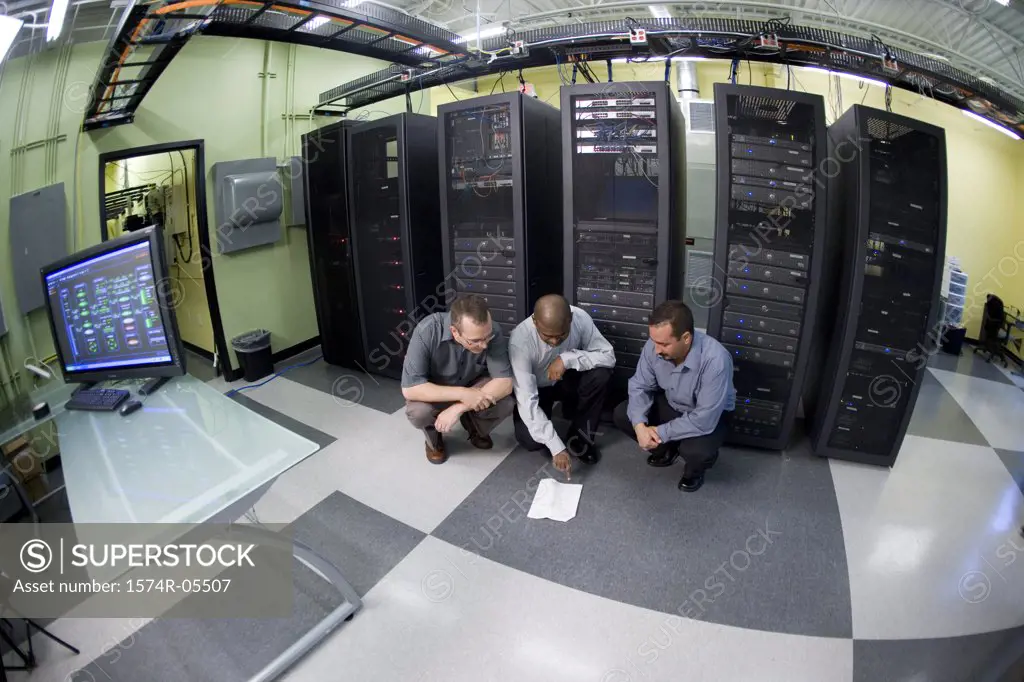 High angle view of three technicians crouching in front of a network server