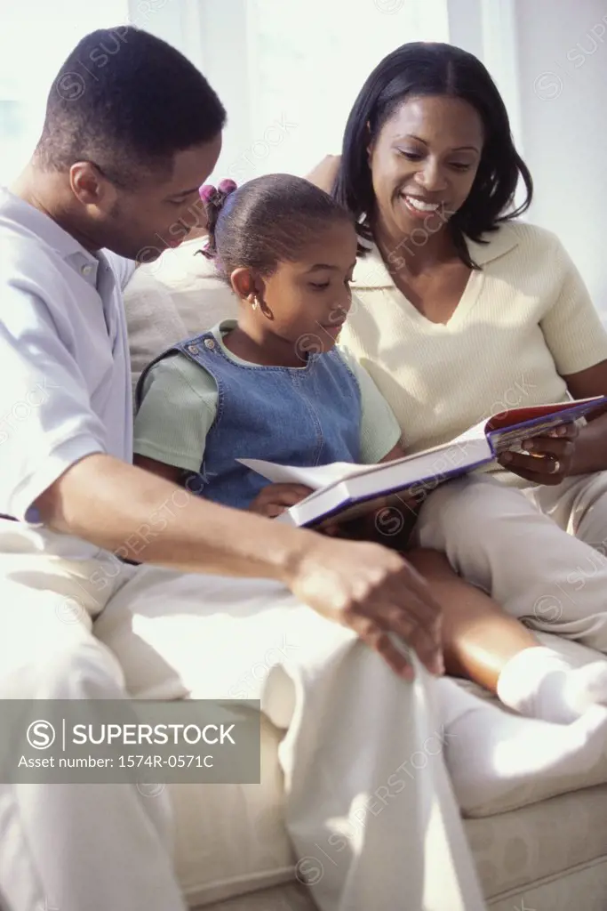 Father and mother sitting on a sofa with their daughter reading a book
