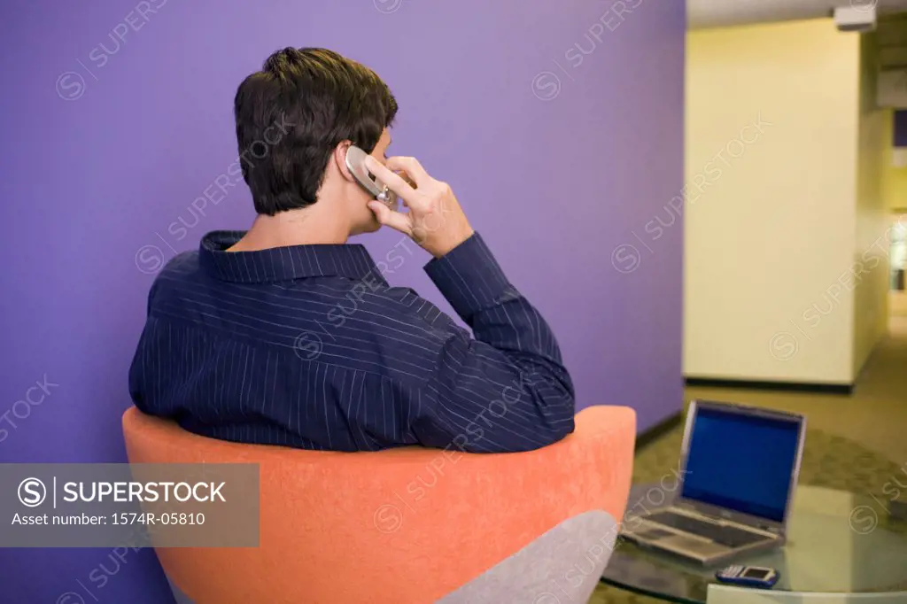 Rear view of a businessman using a mobile phone sitting in front of a laptop