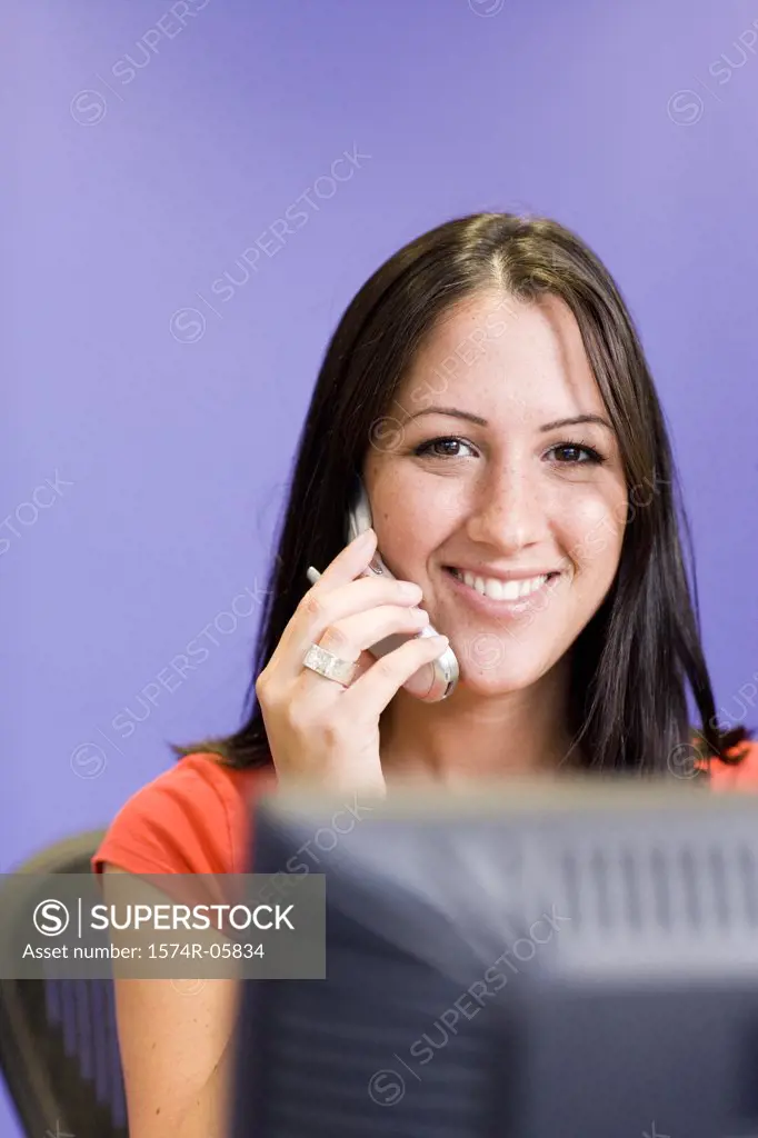 Portrait of a businesswoman sitting in front of a computer monitor talking on a mobile phone