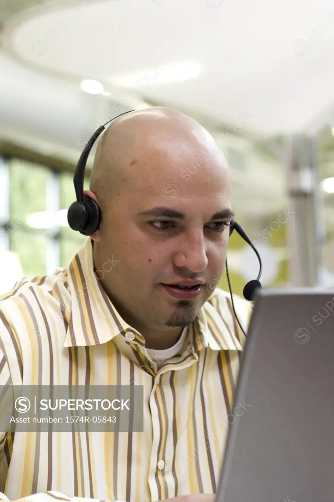 Close-up of a male customer service representative wearing a headset sitting in front of a laptop