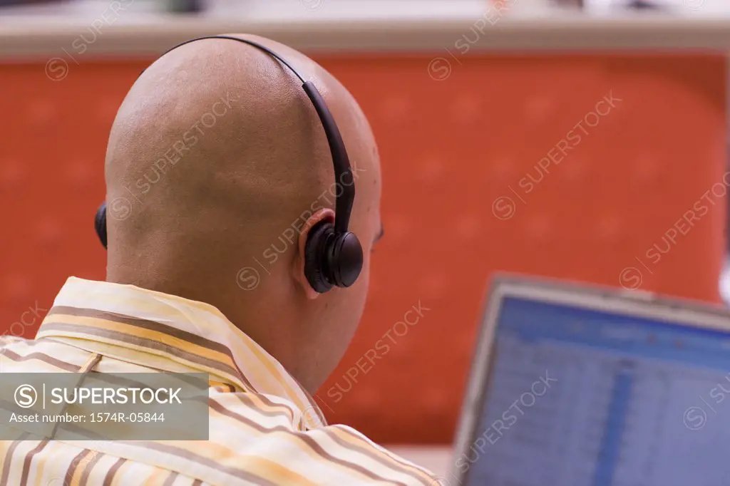 Rear view of a male customer service representative wearing a headset sitting in front of a laptop