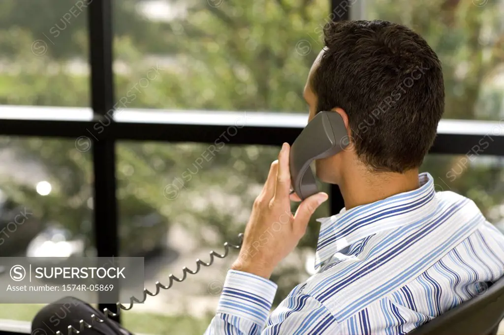 Rear view of a businessman sitting in an office using a telephone