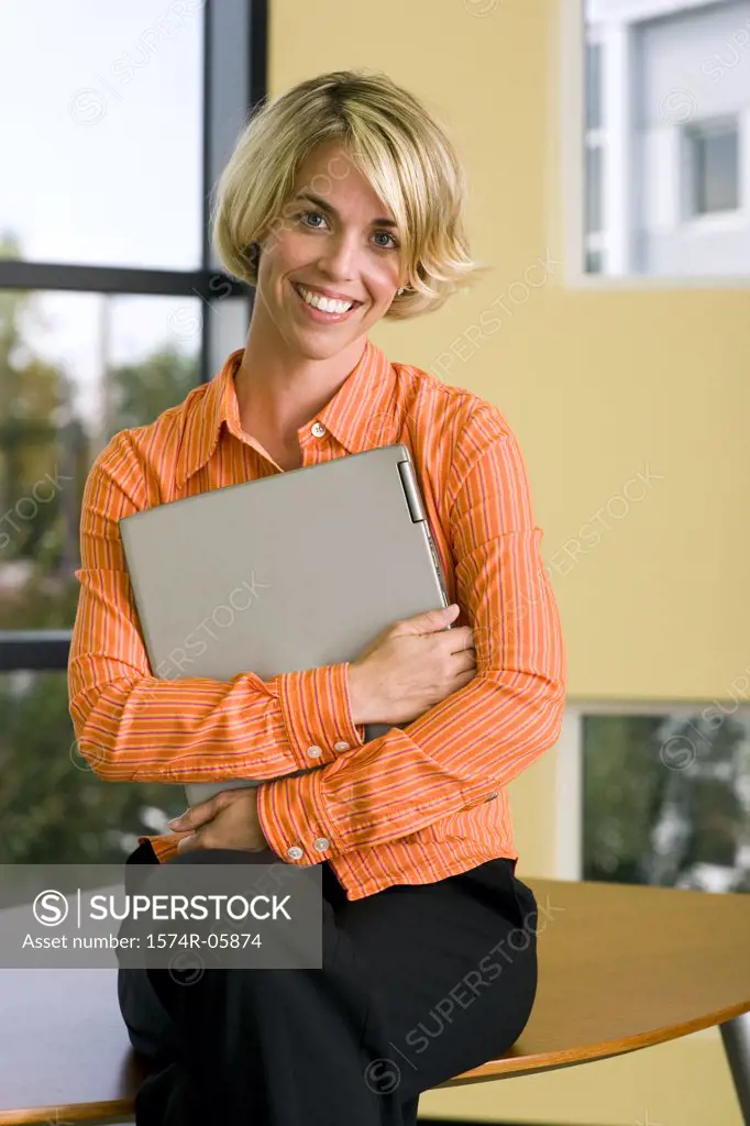 Portrait of a businesswoman sitting on a desk holding a laptop