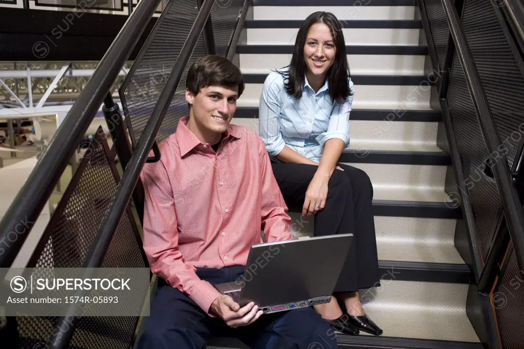 Portrait of a businessman and a businesswoman sitting on stairs in front of a laptop