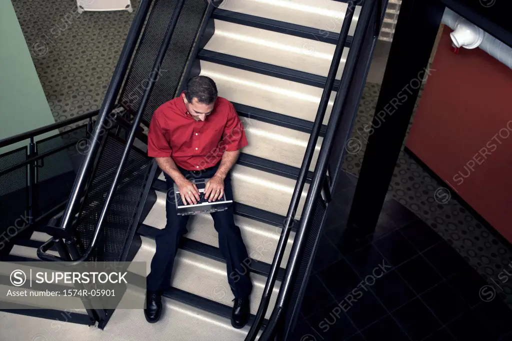 High angle view of a businessman sitting on stairs working on a laptop