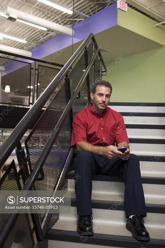 Portrait of a businessman sitting on stairs holding a mobile phone