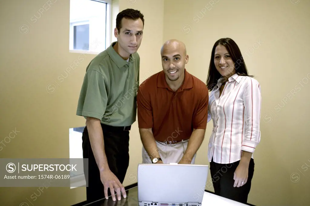 Portrait of two businessmen and a businesswoman standing in front of a laptop