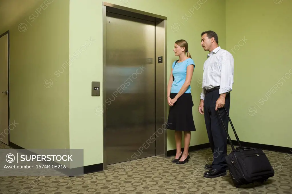 Businessman and a businesswoman standing near an elevator