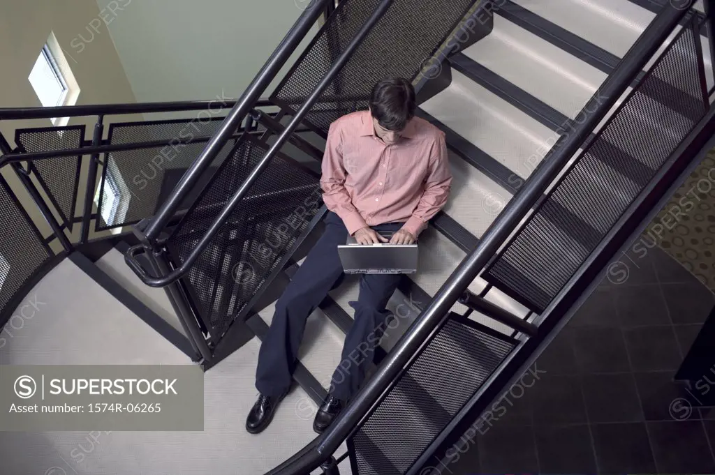 High angle view of a businessman sitting on a staircase working on a laptop