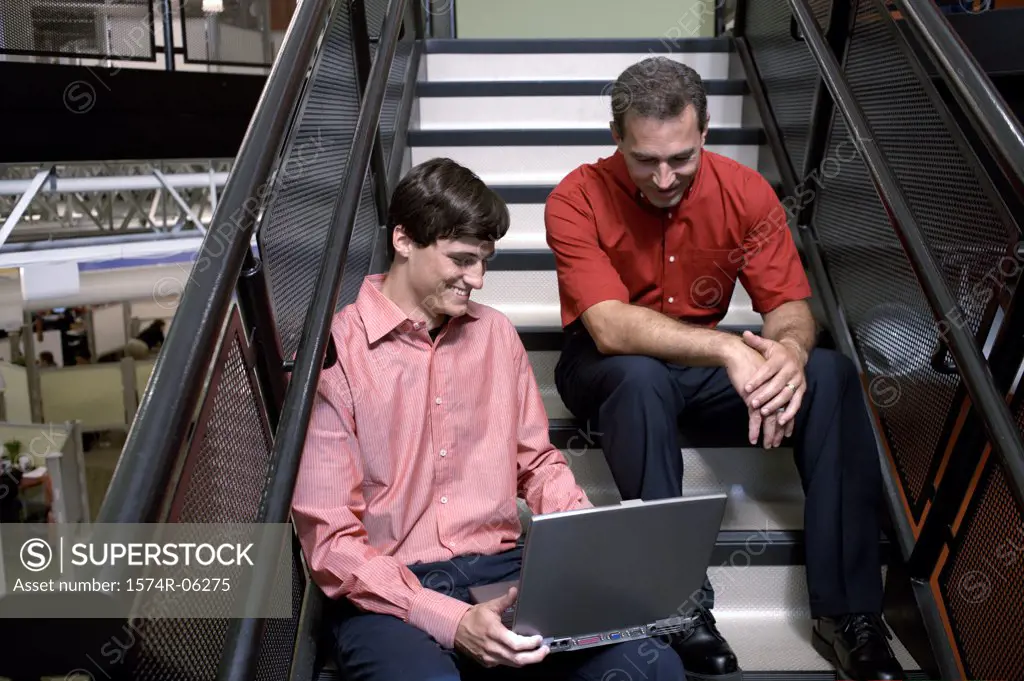 Two businessmen sitting on stairs working on a laptop