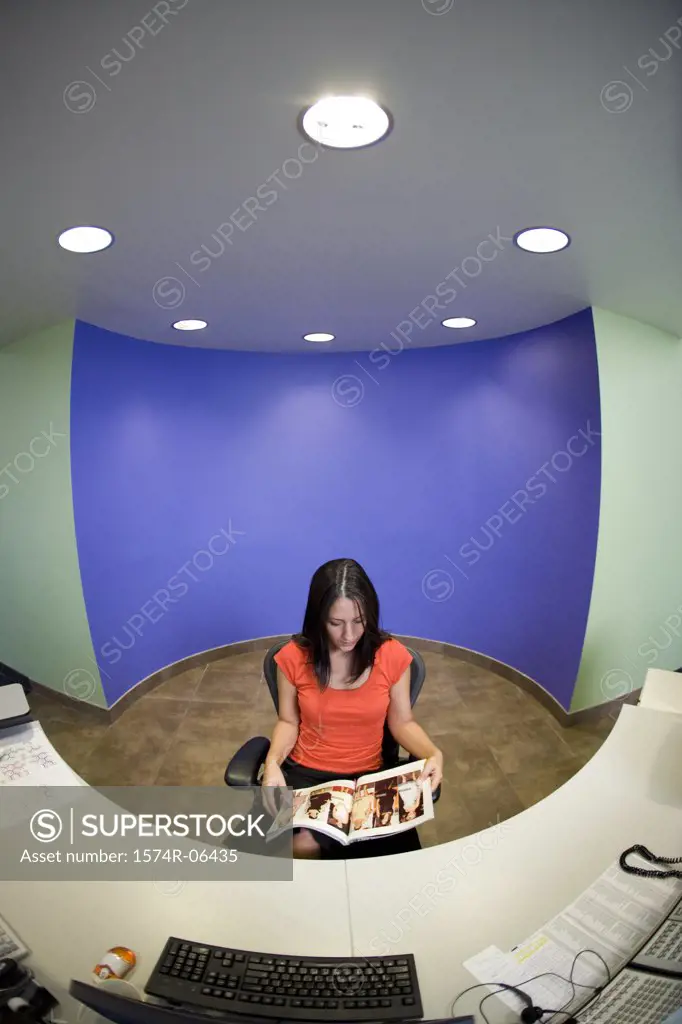 High angle view of a businesswoman sitting in a chair reading a magazine in an office