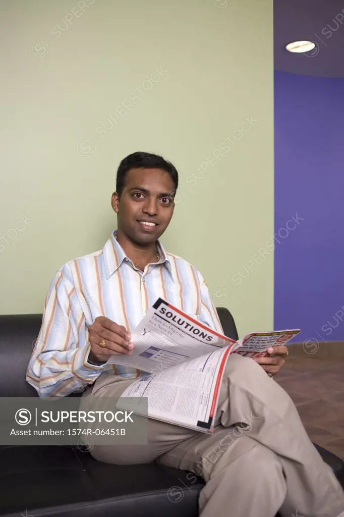 Portrait of a businessman sitting on a couch reading a magazine in an office