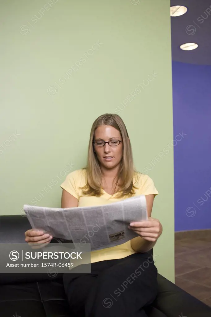 Businesswoman sitting on a couch reading a newspaper in an office