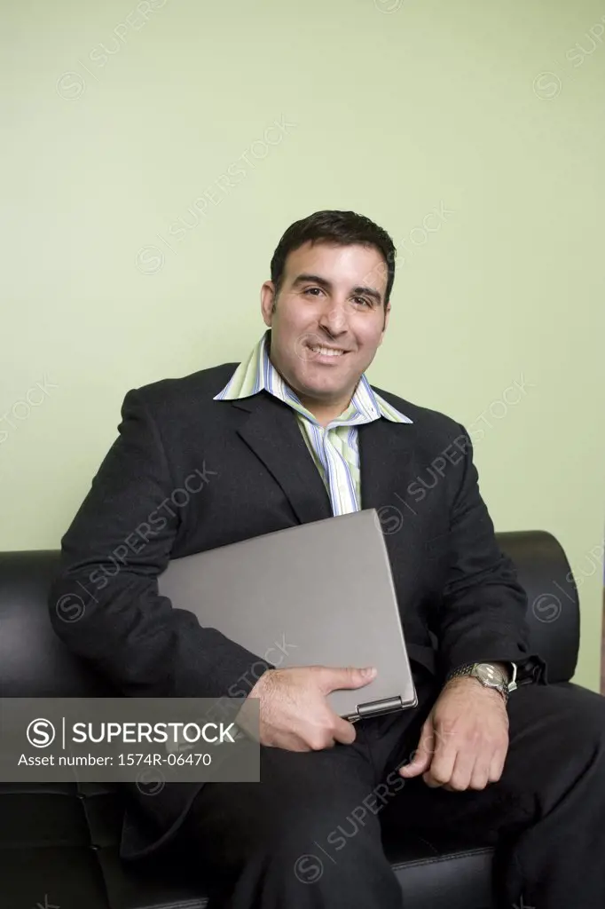 Portrait of a businessman sitting on a couch in an office holding a laptop