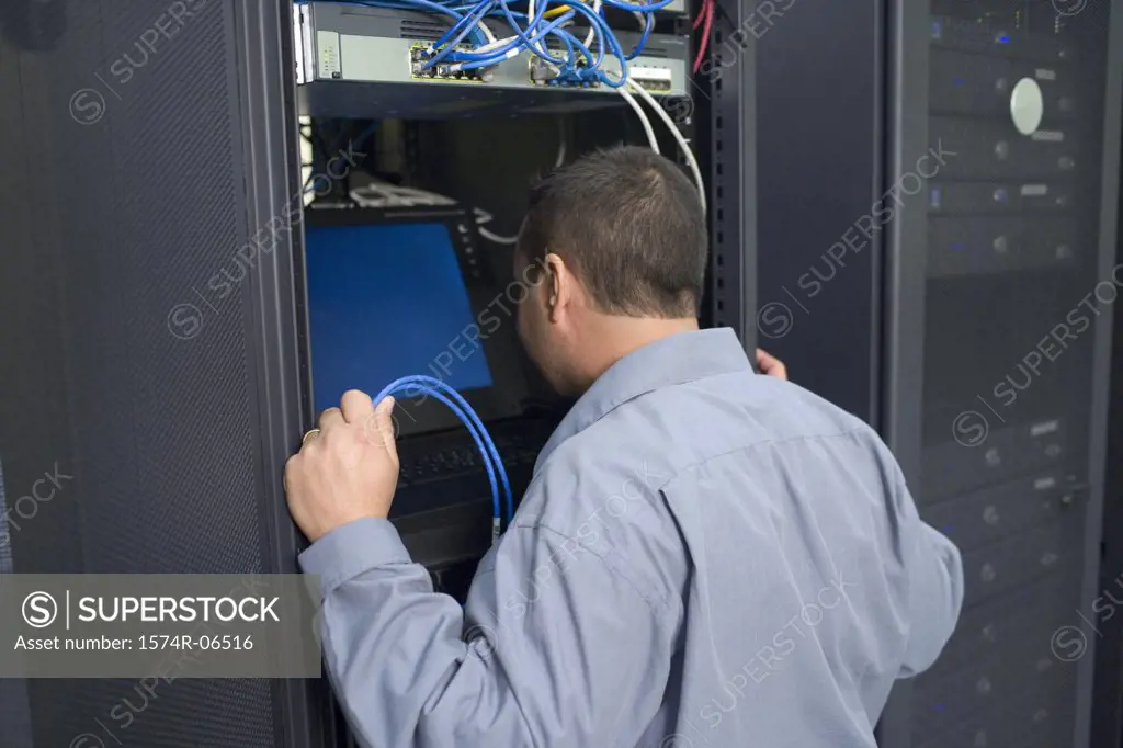 Rear view of a technician looking at a computer monitor in a server room