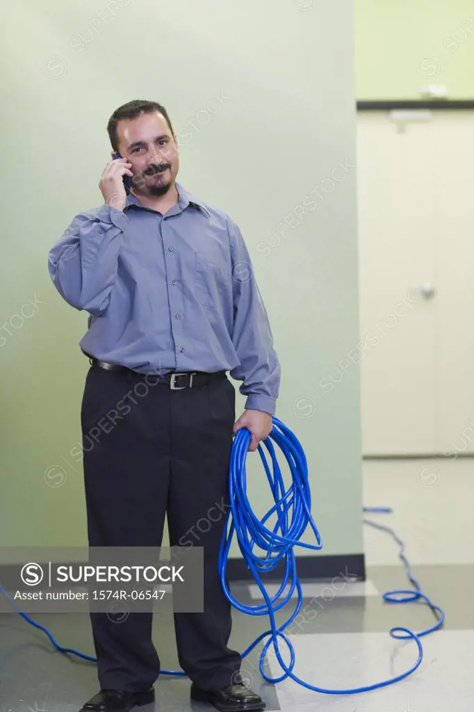 Portrait of a technician holding computer cables talking on a mobile phone
