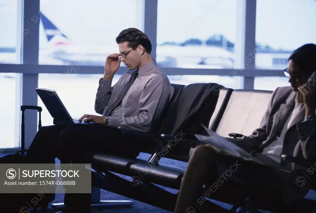Side profile of a businessman and a businesswoman sitting in an airport lounge