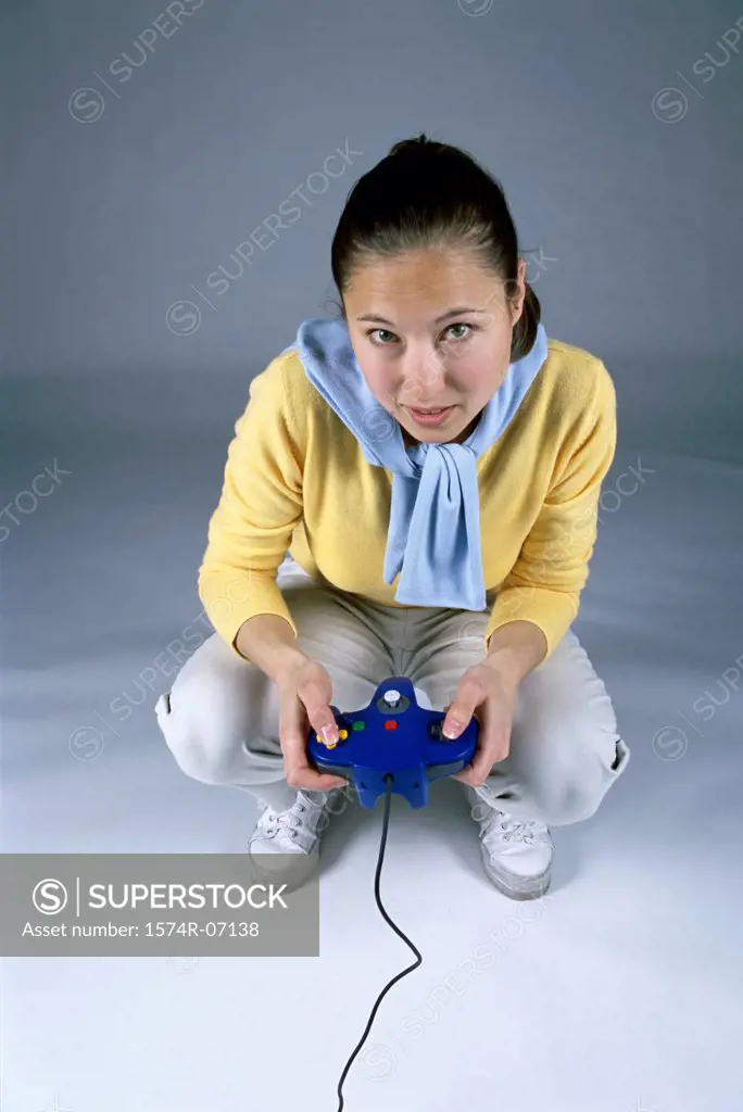 High angle view of a young woman squatting and holding a game joystick