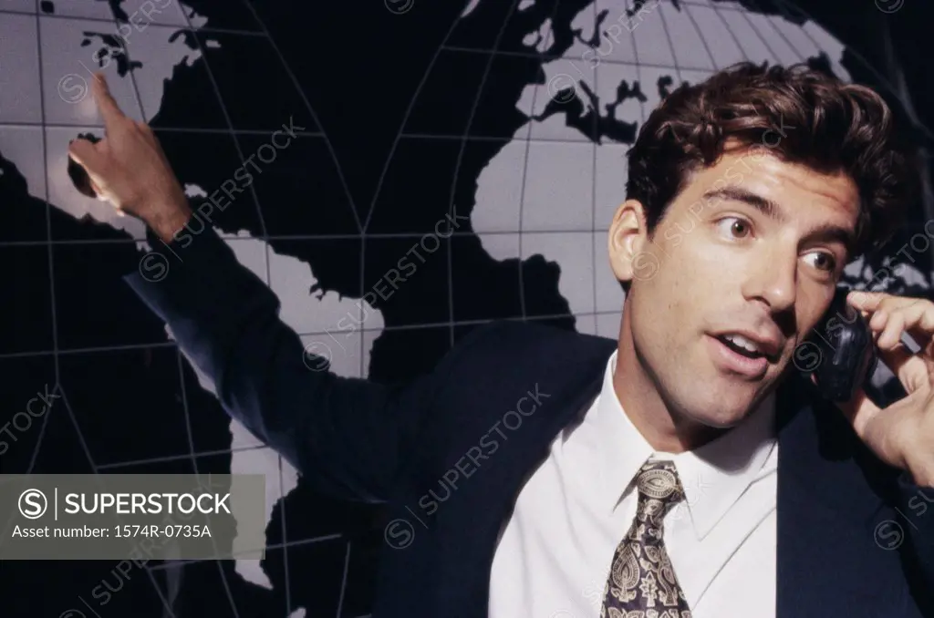 Businessman talking on a mobile phone while pointing to a world map