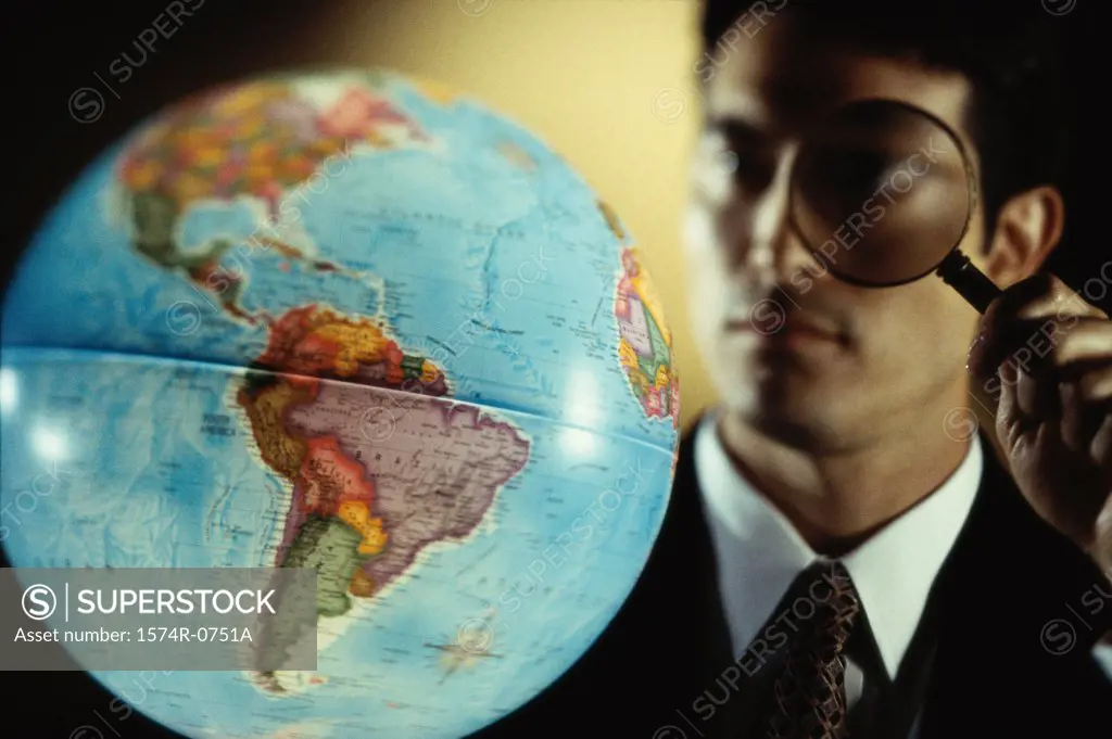 Close-up of a businessman looking through a magnifying glass at a globe