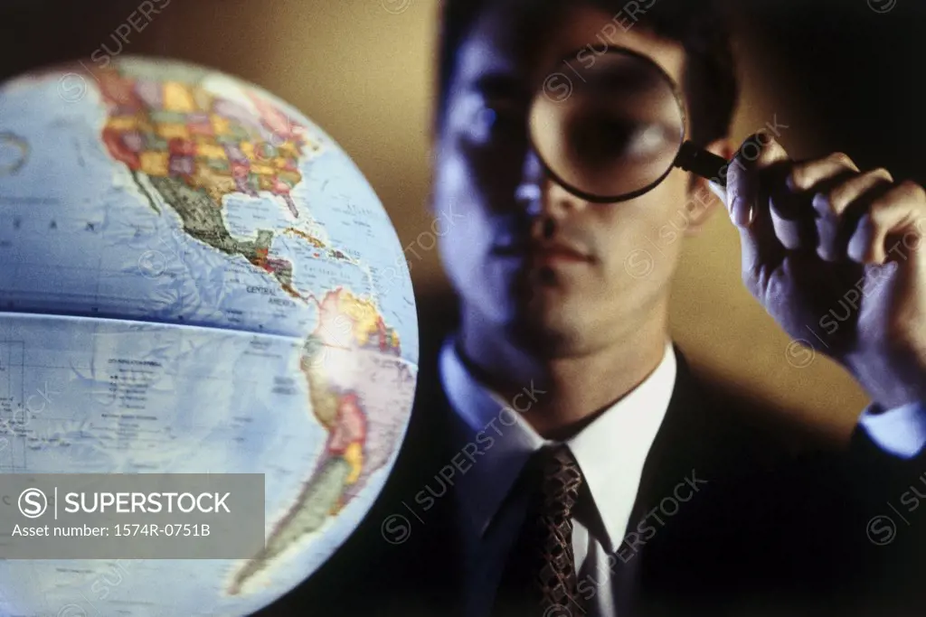 Close-up of a businessman looking at a globe through a magnifying glass