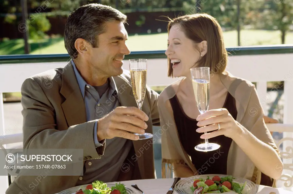 Mid adult couple sitting at a table outdoors toasting with champagne