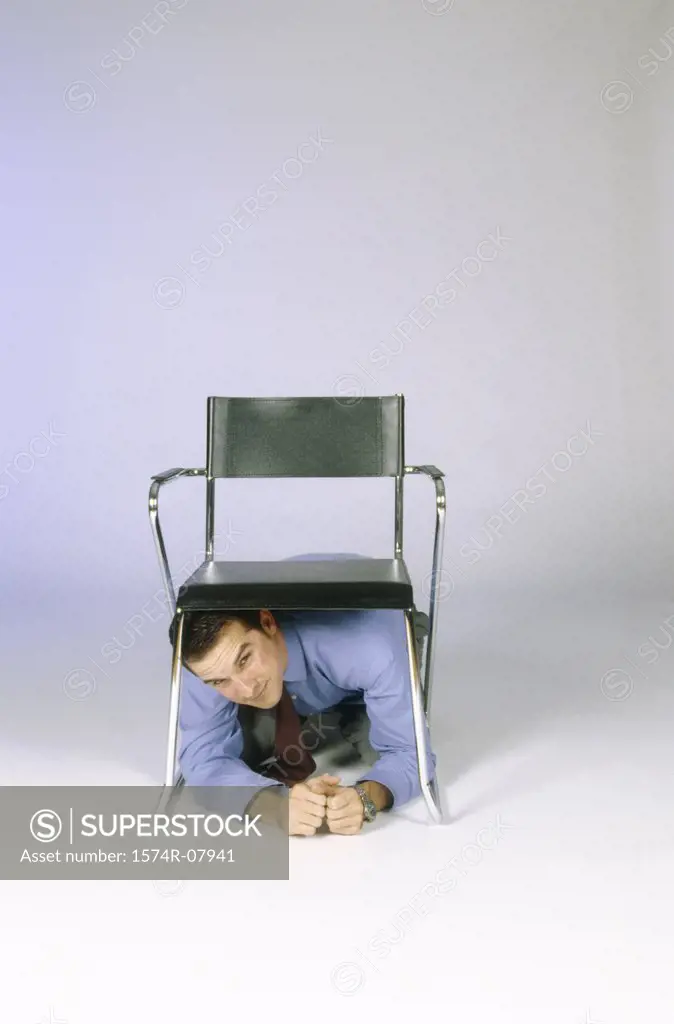 Businessman crouching under a chair