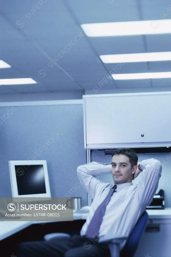 Portrait of a businessman seated at an office desk with his hands behind his head