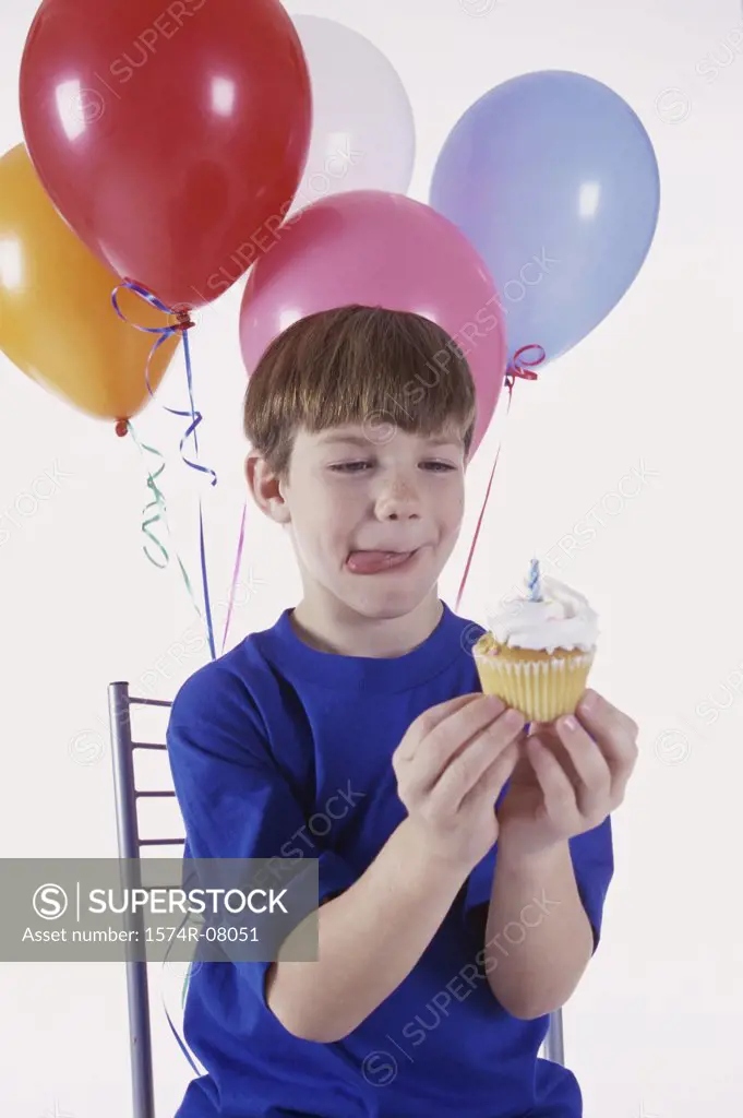 Boy holding a cupcake with balloons behind him