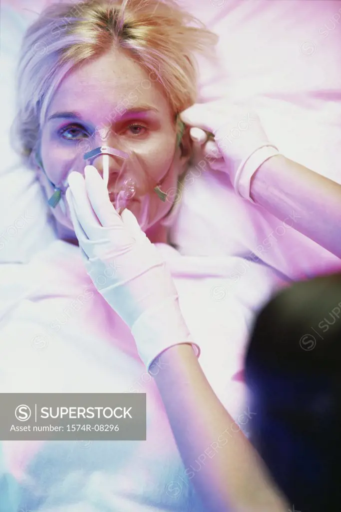 Mid adult woman lying down with a person holding an oxygen mask over her face