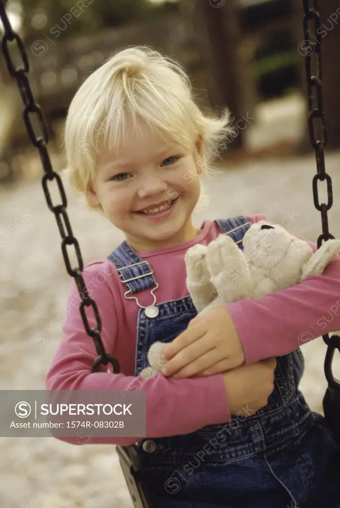 Portrait of a girl sitting on a swing holding a teddy bear