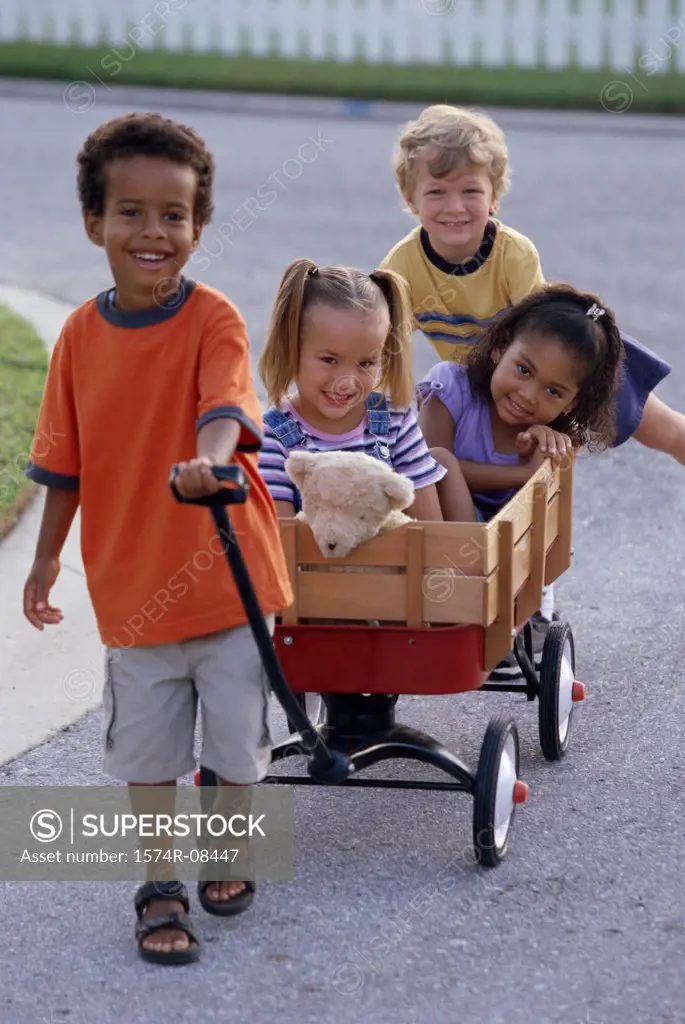 Portrait of two boys and two girls playing with a push cart