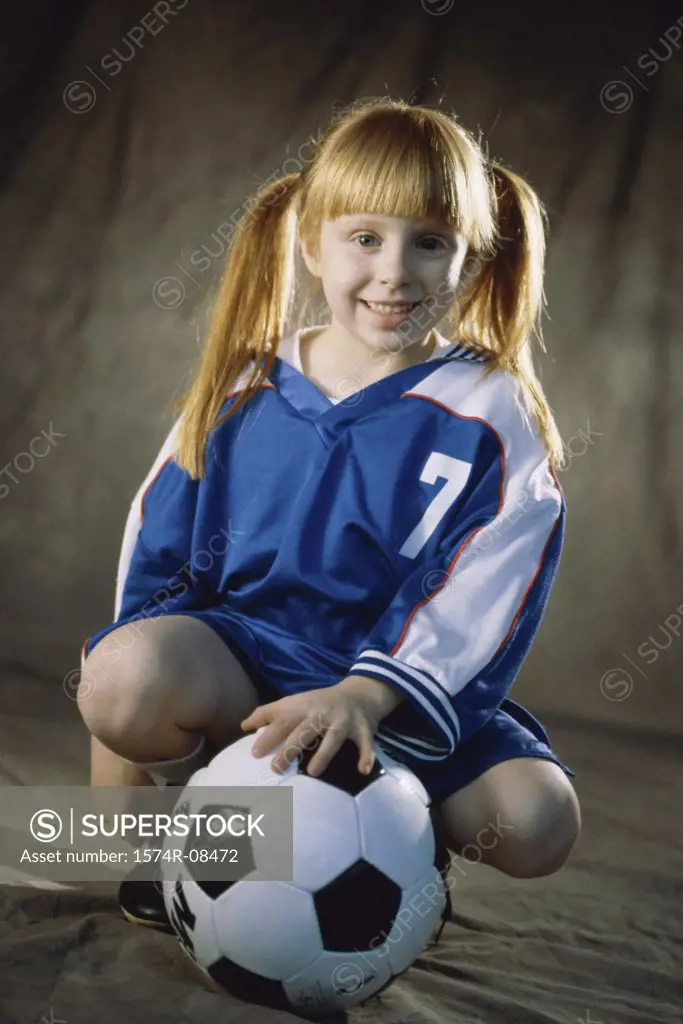 Portrait of a girl squatting in front of a soccer ball