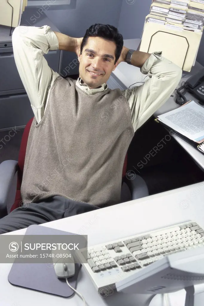 Portrait of a businessman seated at an office desk with his hands behind his head