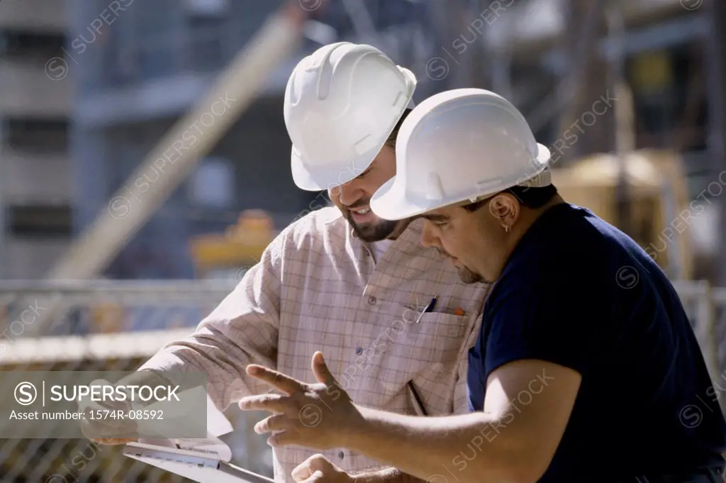 Two foremen working holding blue prints standing at a construction site