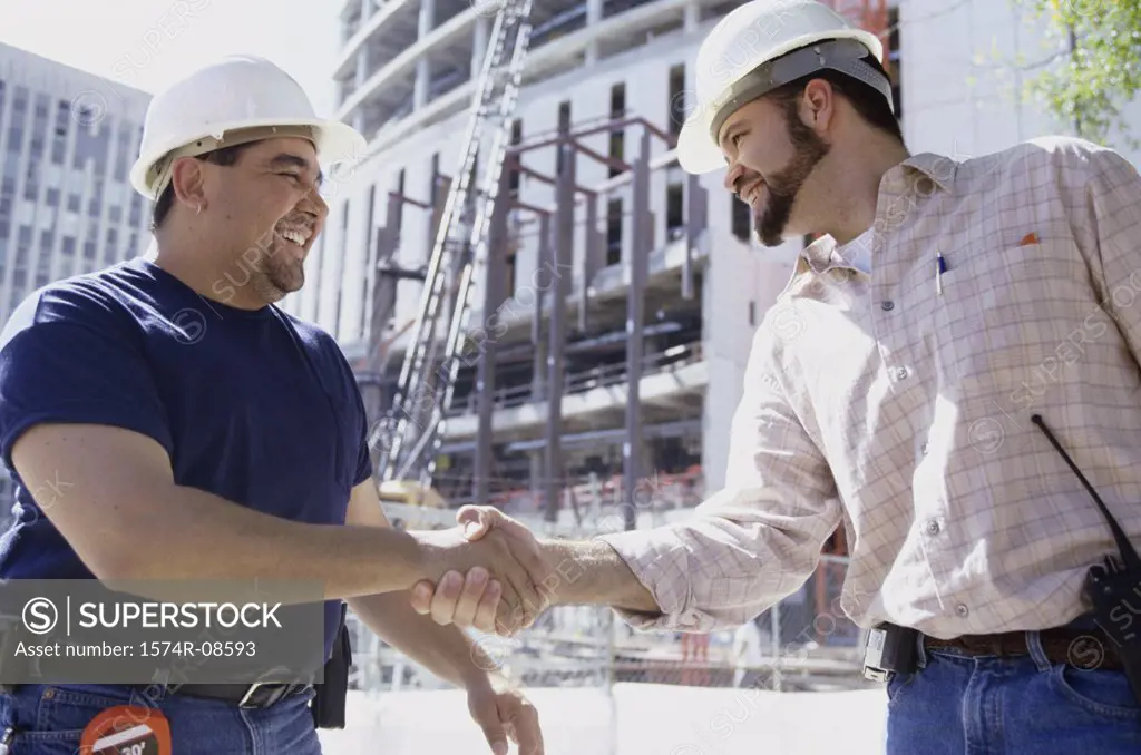 Low angle view of two foremen shaking hands standing at a construction site