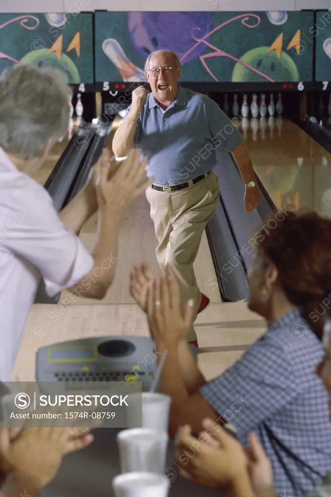 Senior man at a bowling alley with a senior couple applauding him