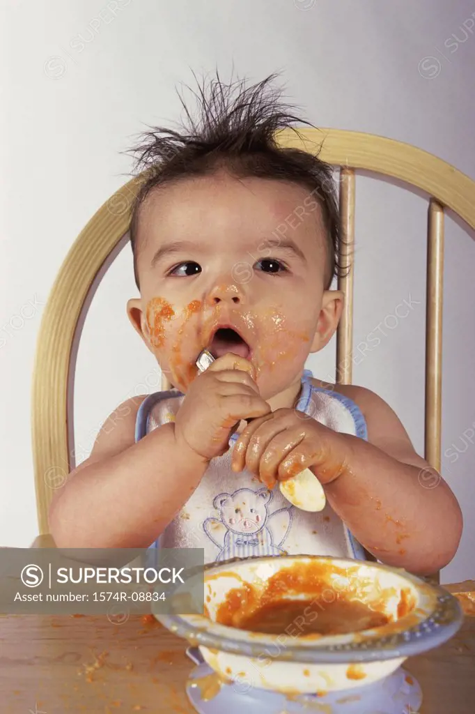 Close-up of a baby boy sitting in a high chair holding a spoon
