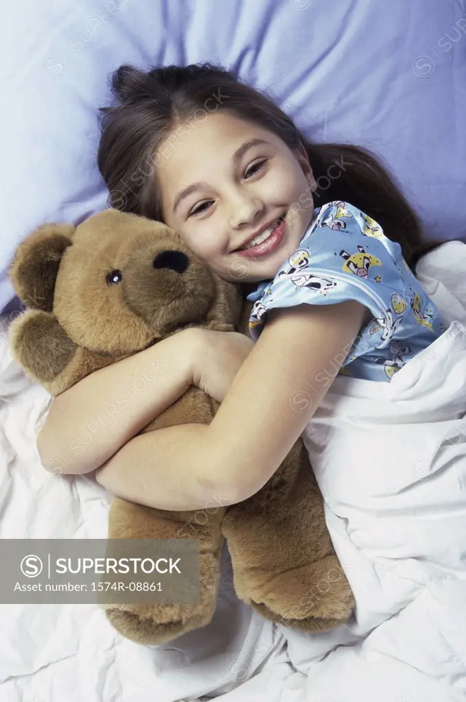 Portrait of a girl lying in bed holding a teddy bear