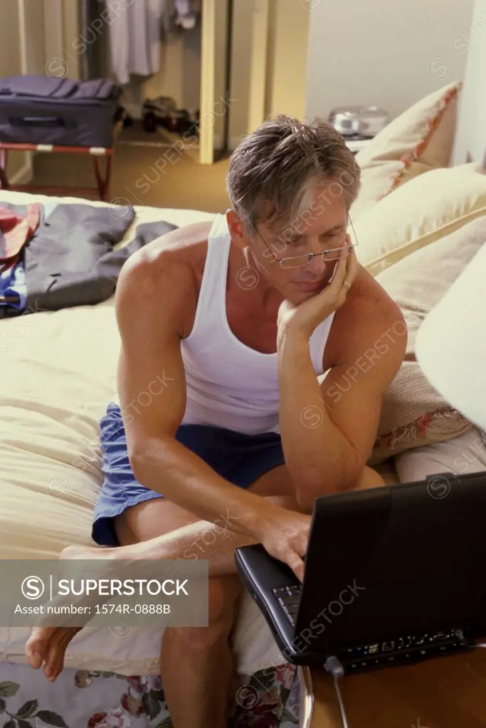 Mature man sitting on the bed and using a laptop