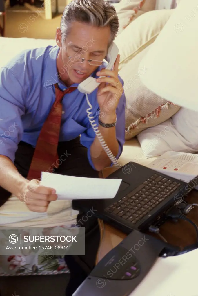 Mature man sitting on the bed and talking on a landline phone
