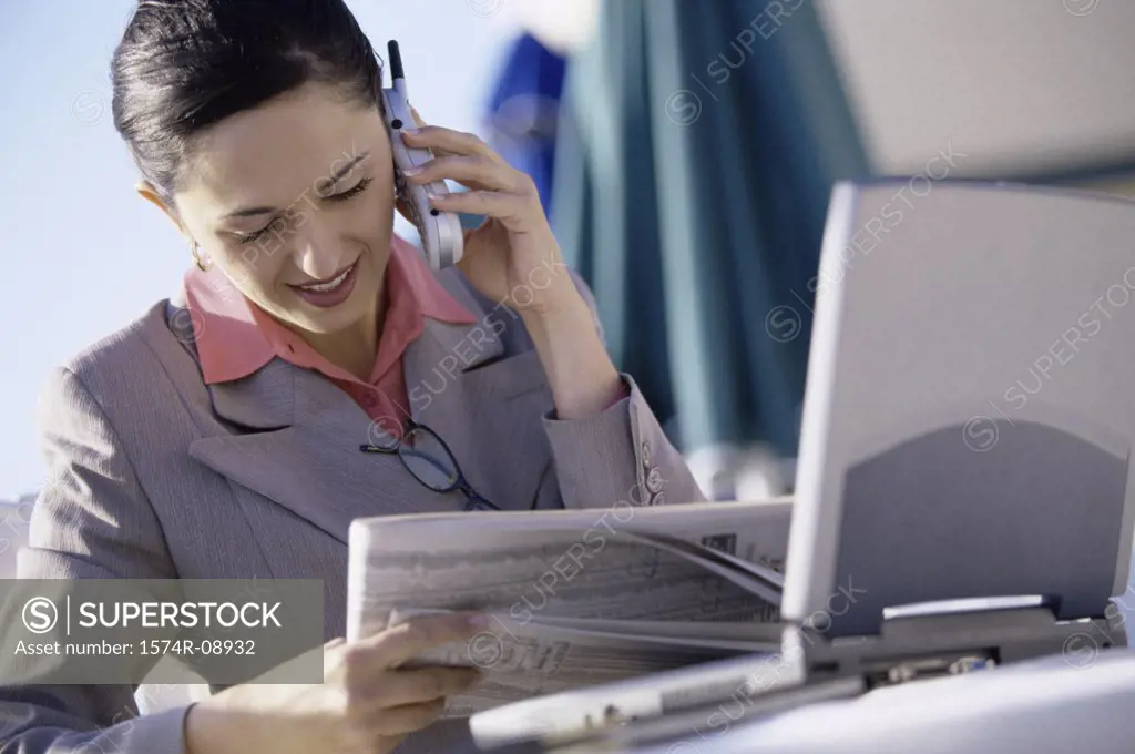 Businesswoman talking on a mobile phone while reading a newspaper
