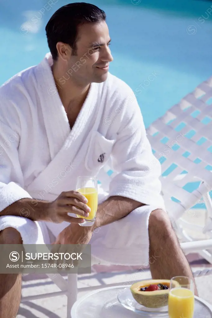 Young man sitting poolside with a glass of orange juice